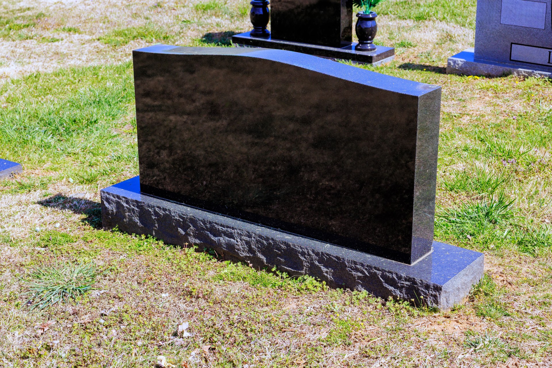 Elegant black gravestone stands in serene cemetery setting under clear blue sky